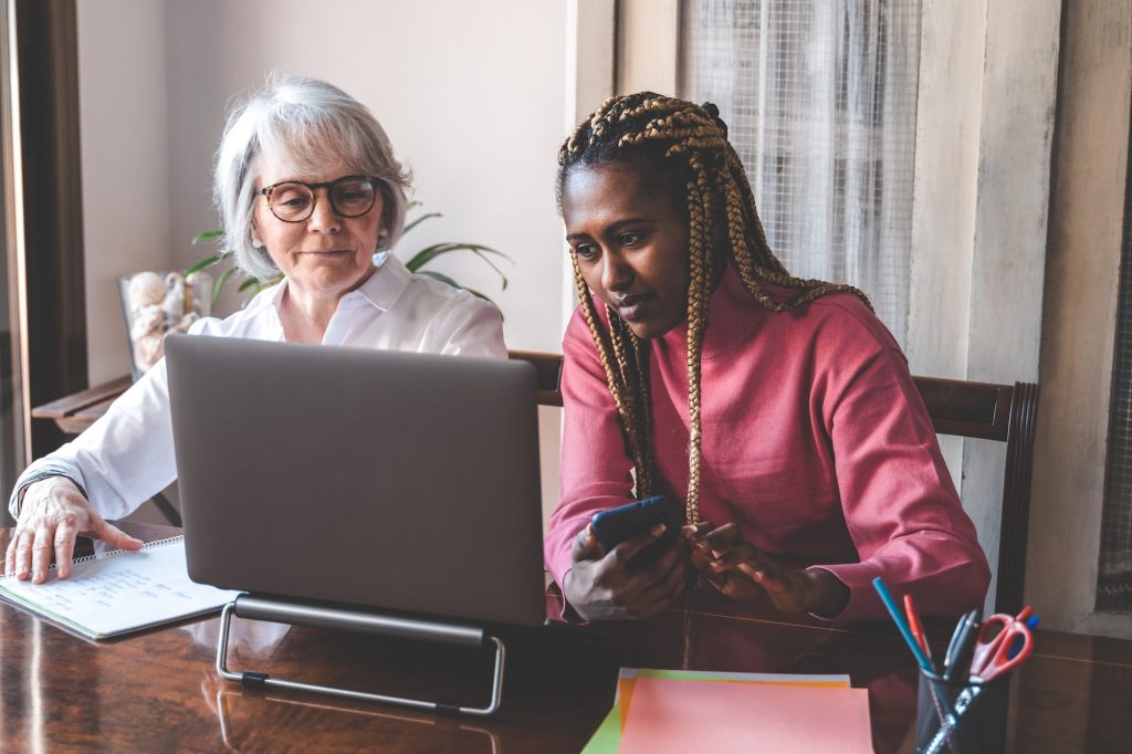 Multi generational senior and young women using laptop computer at home - Focus on african girl face